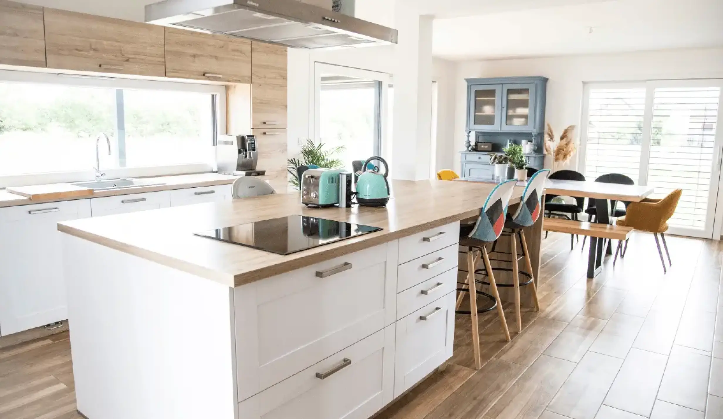 Cuisine moderne ouverte avec îlot central, meubles en bois clair et accès à la salle à manger.