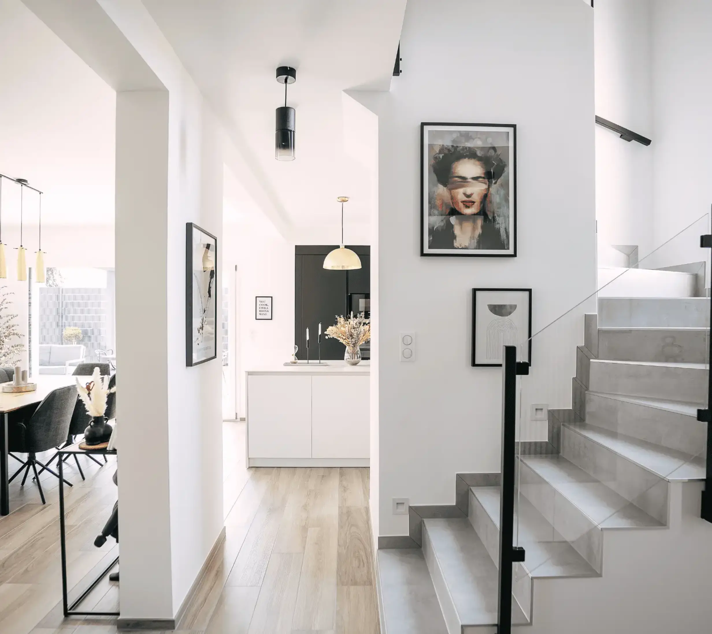 Entrée de maison avec escalier design, couloir lumineux et vue sur cuisine moderne.