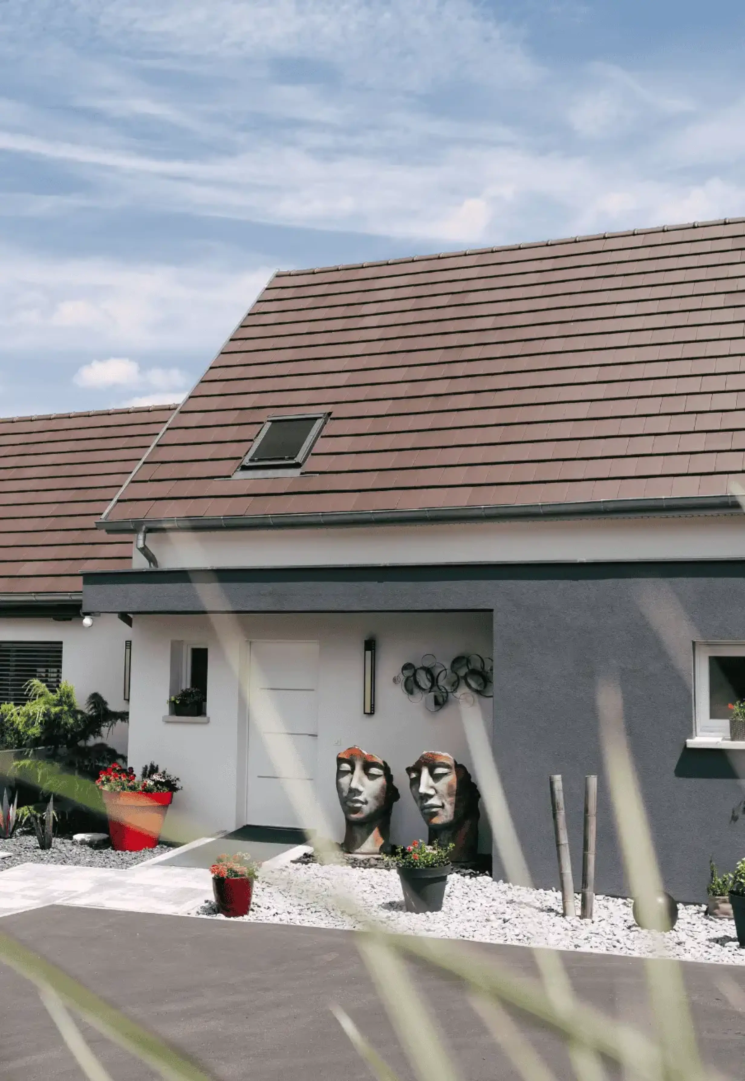 Entrée de maison décorée avec sculptures et végétation sur graviers blancs