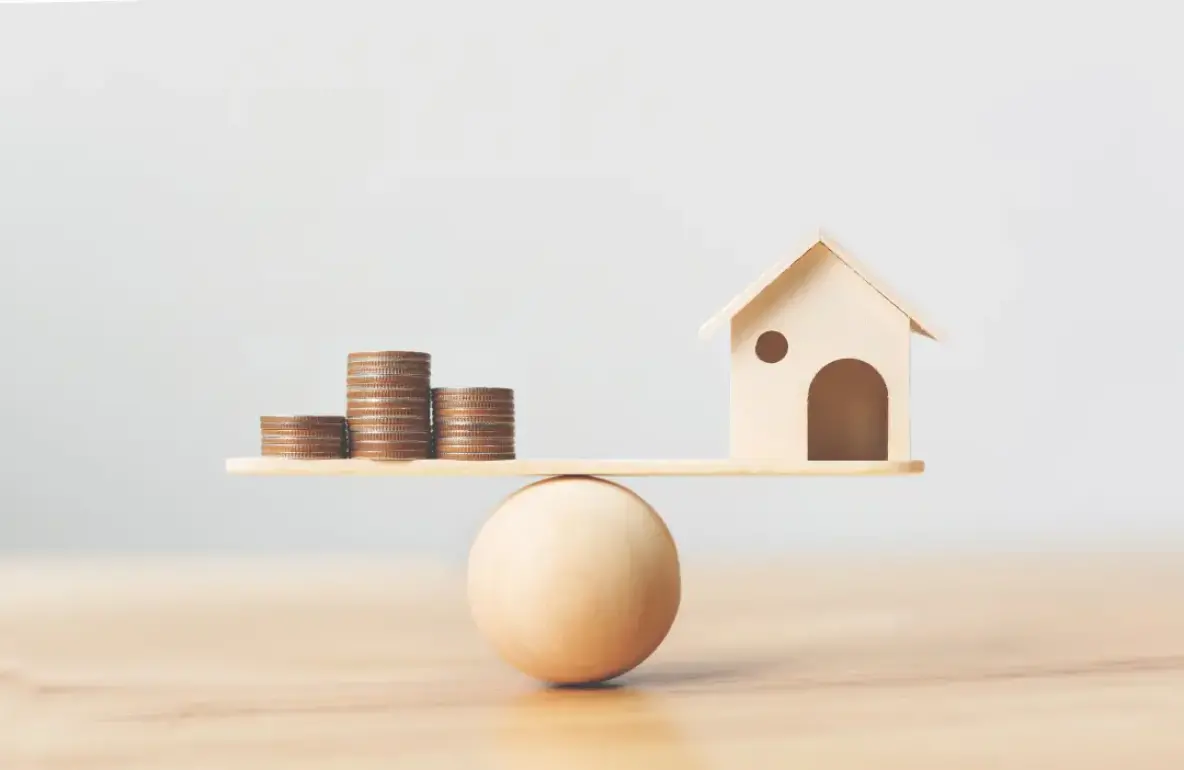 Balance avec une maison miniature et des pièces de monnaie.